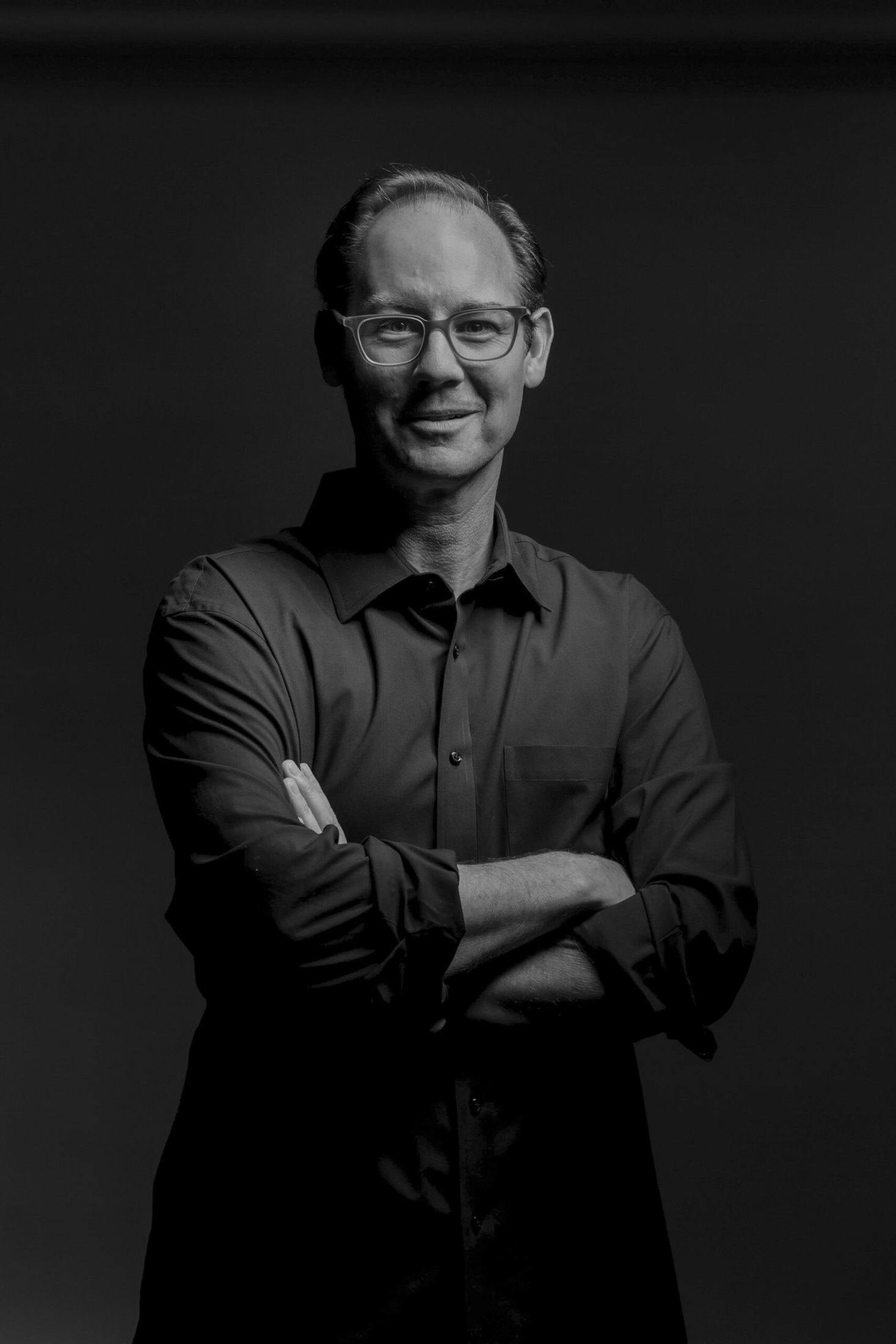 Travis Woods standing with arms crossed in a black and white studio portrait