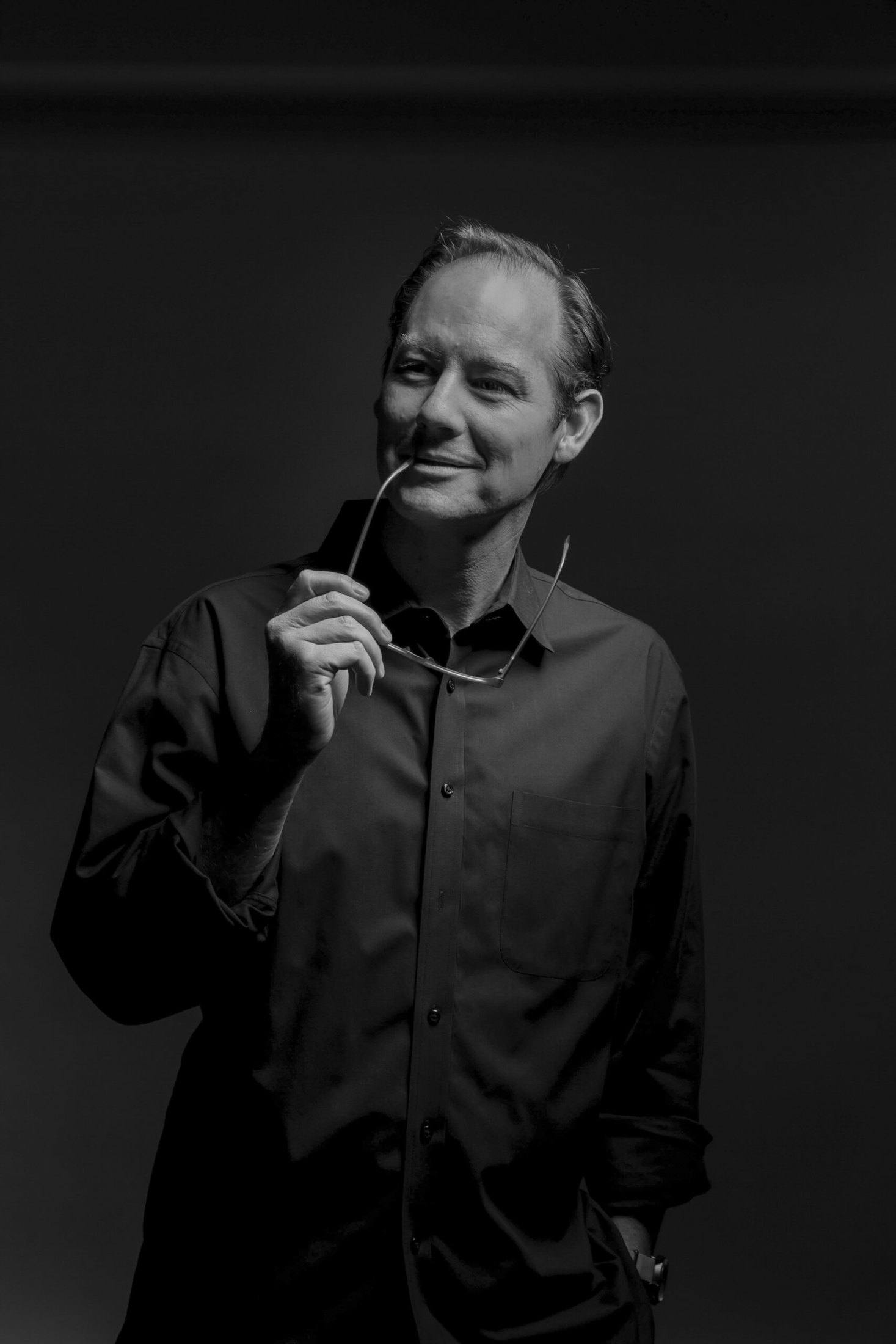 Travis Woods holding his glasses in a black and white studio portrait