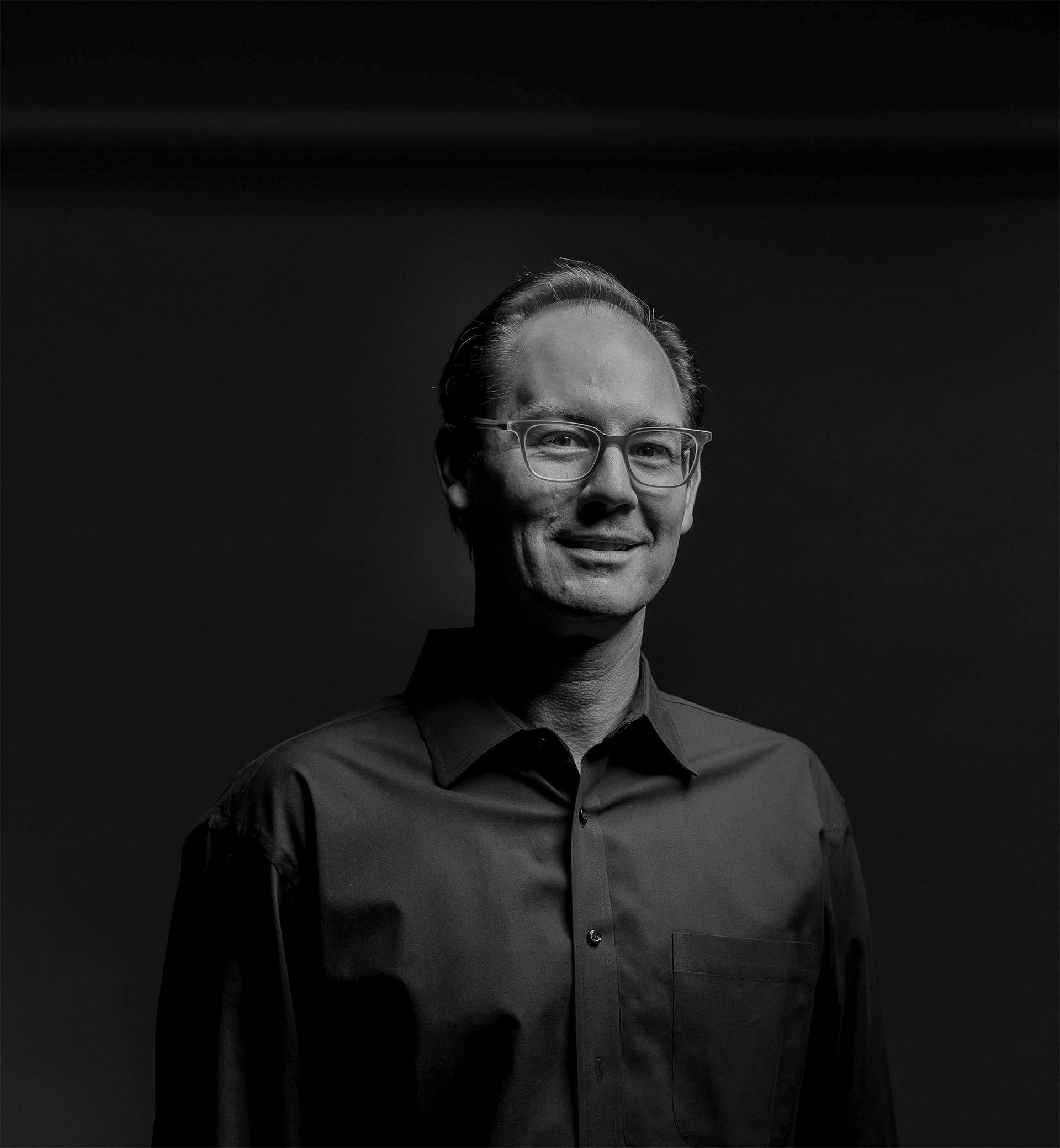 Black and white studio portrait of Travis Woods, smiling, in a dark button-down shirt